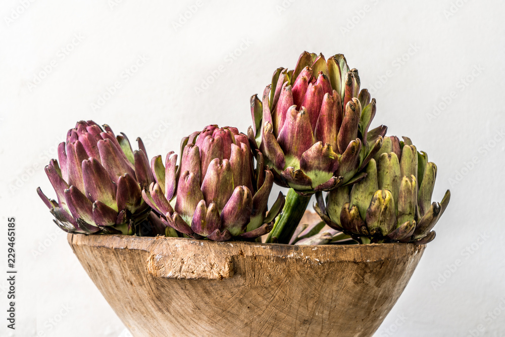 artichokes inside a wooden bowl with a white wall background artichokes inside a wooden bowl with a white wall background