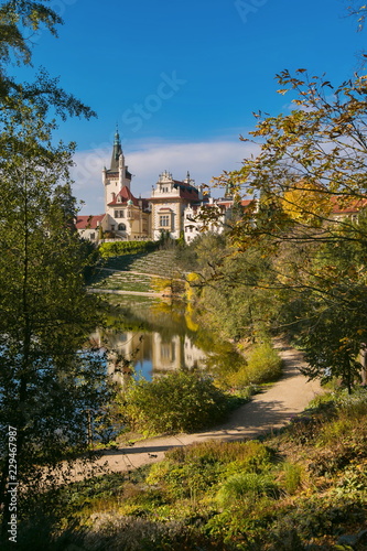 Vertical image of romantic park and famous castle Pruhonice, Czech Republic, Europe, standing on a hill above lake, colorful sunny autumn day, blue sky, footpath along lake, reflection, vertical image