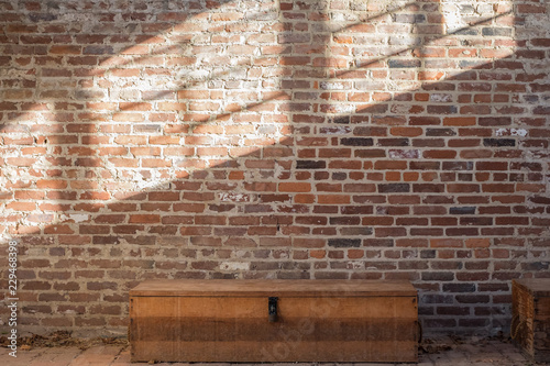 OLD RED / ORANGE RUSTIC BRICK WALL WITH SHADOW OF WINDOWS AND NATURAL LIGHT / AND WOODEN BOX WITH LOCK ON THE FLOOR