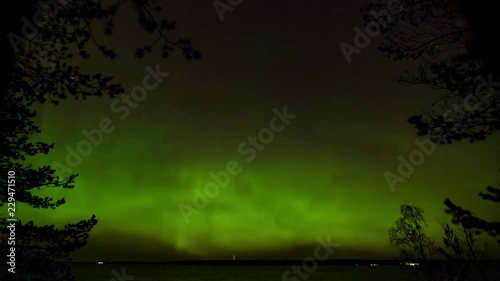 Time lapse of Aurora borealis above lake getting weaker. Framed by trees in the foreground. photo