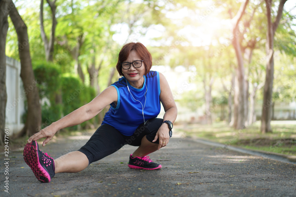 © kromkrathog - Senior asian woman stretch muscles at park and listening to music. Athletic senior exercising together outdoor. Fit senior runners stretching before running outdoors.