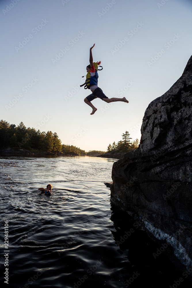 Silhouette of kids jumping off cliffs while on a canoe trip