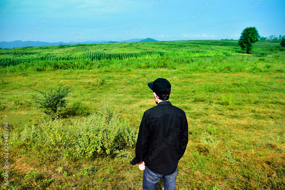 Man standing on green meadow with sunlight in the morning. With beautiful views of nature. Rear view Green color Plant Field Land landscape Man standing on green meadow with sunlight in the morning. With beautiful views of nature. Rear view Green color Plant Field Land landscape