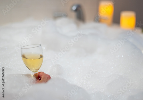 woman holding a glass of wine in bubble bath with candles