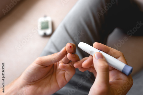 Handsome stylish young teen caucasian white brunette guy man european taking a blood sample with a glucometer to measure sugar level lancet on finger diabetes  glycemia meter top first view shot