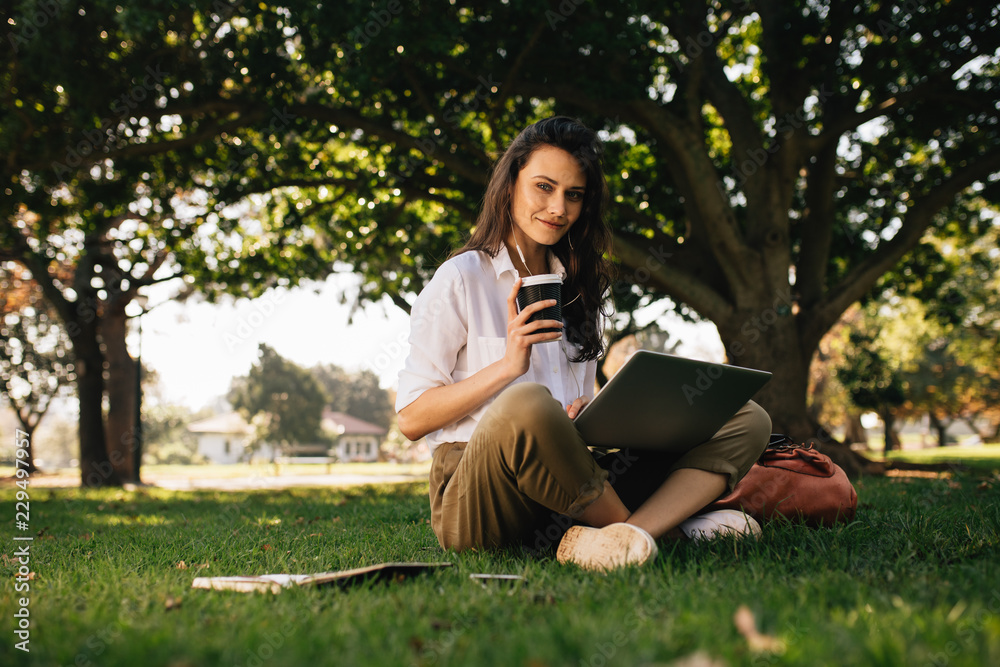 Beautiful woman sitting at park with a coffee and laptop Beautiful woman sitting at park with a coffee and laptop