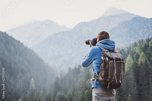 Young cheerful man photographer taking photographs with digital camera in a mountains. Travel and active lifestyle concept