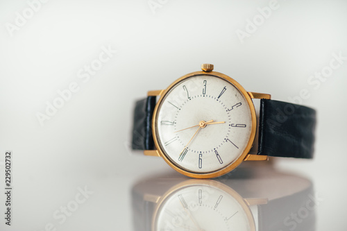 Vintage golden watch laying on white glossy surface with reflection. Copy space. Black leather strap. 