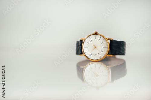 Vintage golden watch laying on white glossy surface with reflection. Copy space. Black leather strap.
