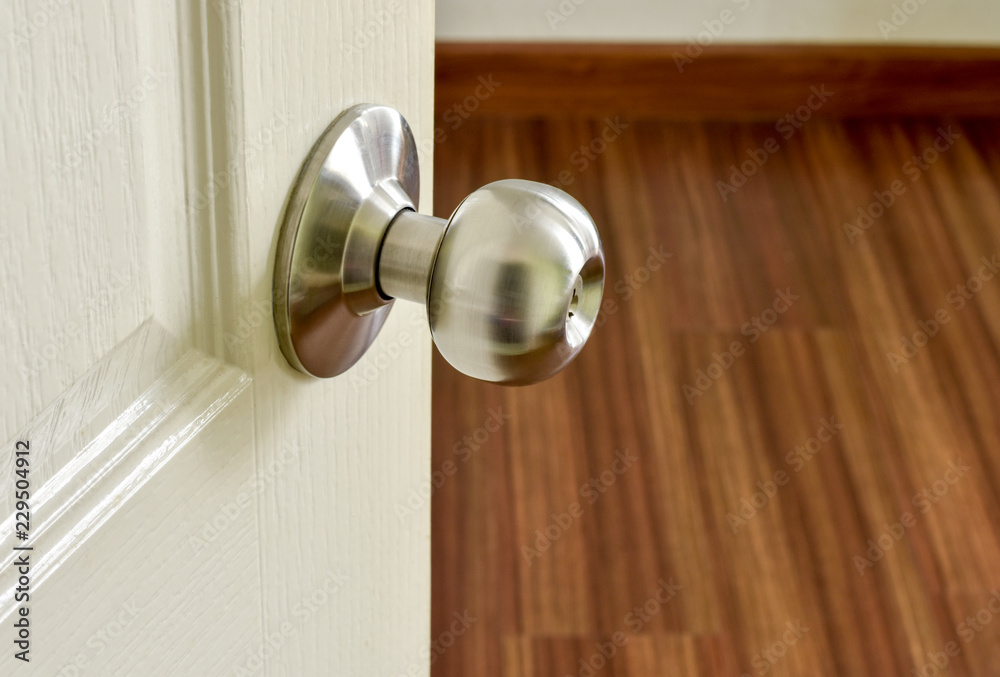 Close up of stainless metal door knob on a white painted door opening into a room. Close up of stainless metal door knob on a white painted door opening into a room.