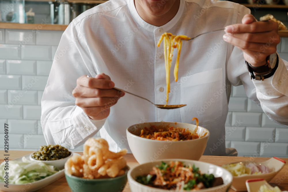 Asian Man eat Thai Food -Khao Soi with pork snack (Thai Noodle Curry Soup with chicken), Nam Prik Num (Green chili dip) and  Hunglei curry (North curry With tender pork) over the wooden table