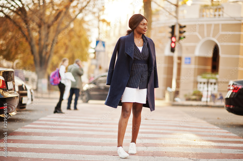 Success stylish african american woman in coat walking at crosswalk.