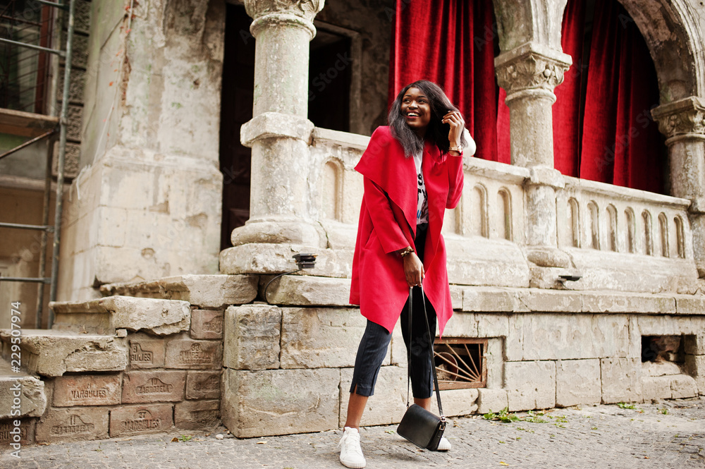 Stylish african american woman in red coat posed against old columns. Stylish african american woman in red coat posed against old columns.