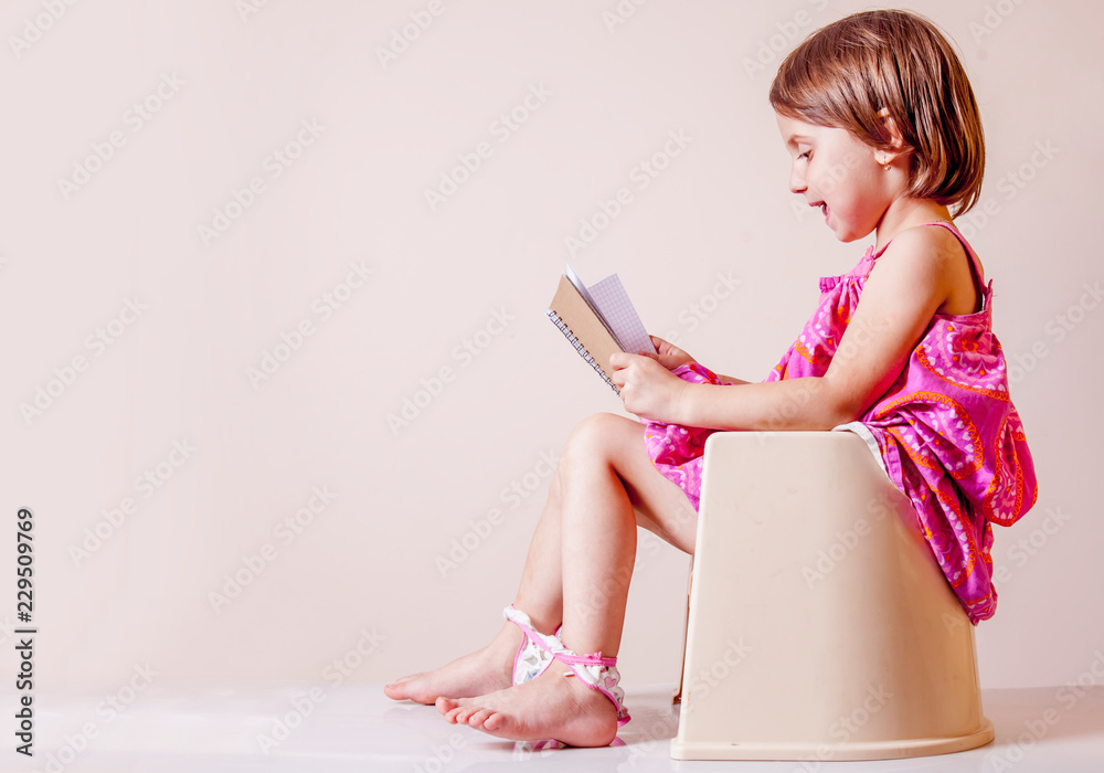 Toilet busy Images. Little cute child girl with notebook sitting on toilet bowl. - obrazy, fototapety, plakaty 