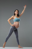 Slim pregnant woman is engaged in fitness isolated on gray background.