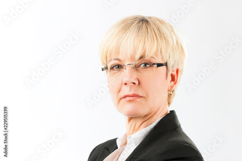 Portrait of a bossy senior woman wearing spectacles and black coat isolated against while background looking at camera