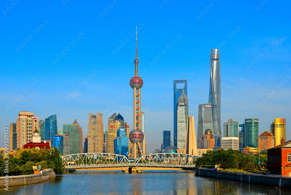 historical Waibaidu bridge with water reflections and colorful blue sky in front of the futuristic modern skyline of Pudong Shanghai, China