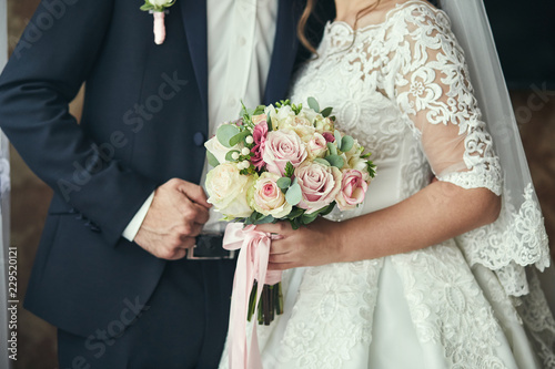 Bride holding a wedding bouquet in the hands standing near groom