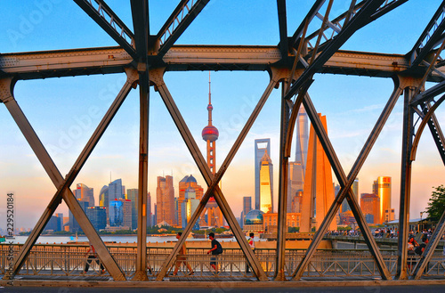 people walking on historical Waibaidu iron bridge in front of the futuristic modern skyline of Pudong Shanghai  China