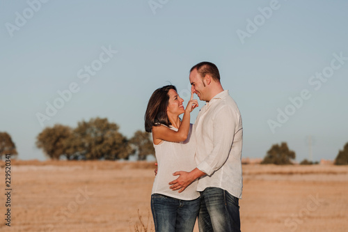 portrait outdoors of a young young pregnant couple in a yellow field. Outdoors family lifestyle. © Eva