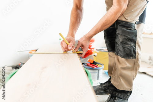 Male worker applies markings to the Board for cutting with a electrofret saw. installing new wooden laminate flooring. concept of repair in house. photo