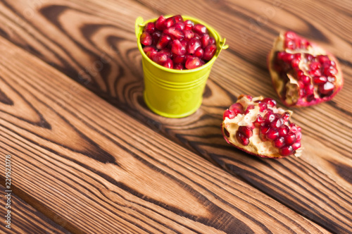 Two halves of fresh ripe red pomegranate with seeds near full green metal bucket of seeds on old brown weathered rustic wooden table