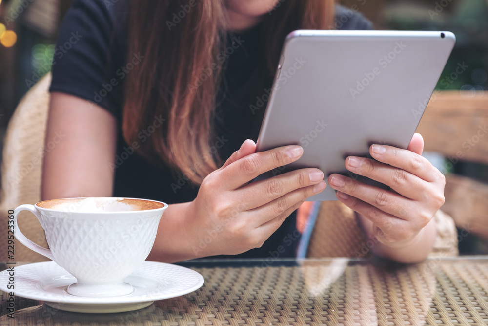 Closeup image of a woman holding and using tablet pc with coffee cup on table in cafe Closeup image of a woman holding and using tablet pc with coffee cup on table in cafe