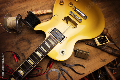 Electric guitar repair. Vintage electric guitar on a guitar repair work shop. Single cutaway solid body guitar, gold color. shallow depth of view, intentionally shot with low key shadows. photo