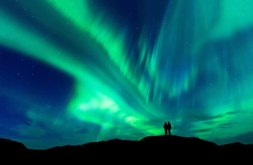 Leinwandbilder Nordlichter Polarlicht Paar Silhouette auf Berggipfel  © basiczto