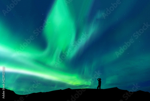 Aurora borealis with silhouette standing man on the mountain.Freedom traveller journey concept