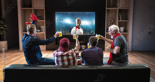 Group of fans are watching a soccer moment on the TV and celebrating a goal, sitting on the couch in the living room.