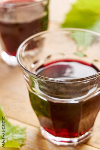 Two informal wine glasses without foot on a table filled with red wine and a green grape leafs. Vertical dutch angle shot with selective focus