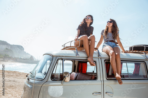 young women with sunglasses sitting on top of minivan roof