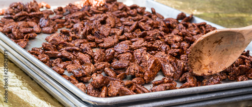 Photo of a wooden spoon and fresh sugar glazed cinnamon roasted pecans on a metal cookie sheet.