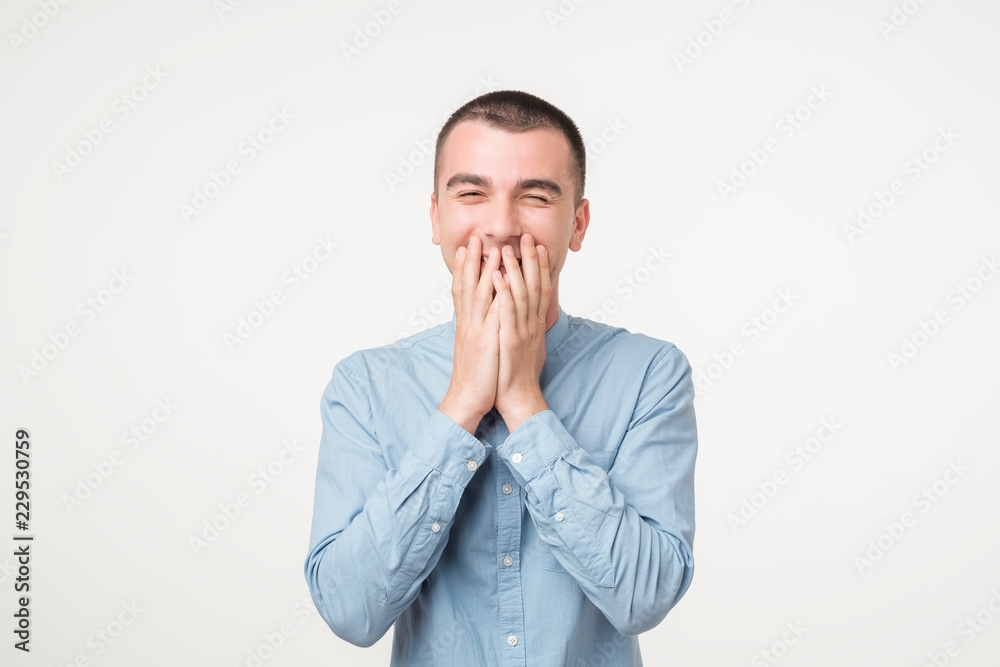 Portrait of young man laughing and covering his mouth with hand over white background. Portrait of young man laughing and covering his mouth with hand over white background.