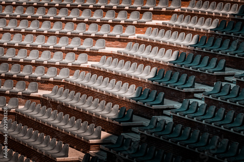 Free unclaimed seats in multiple rows. Sunset photo in empty public arena and concert amphitheatre. Red brick and white travertine structure  gray plastic chairs. 