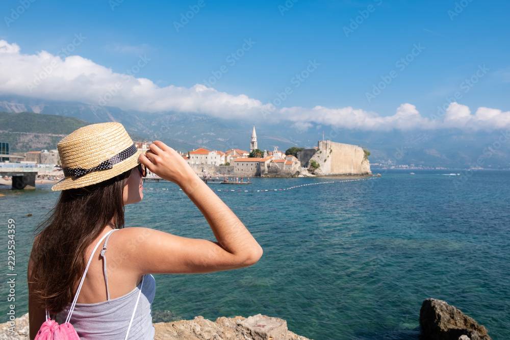 Back view of a young beautiful woman in a hat looking to the old town Budva, Montenegro