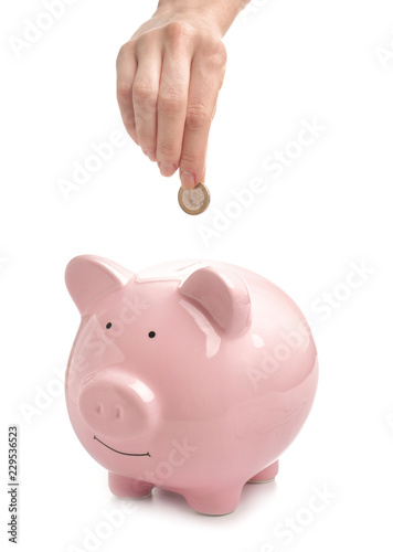 Woman putting coin into piggy bank on white background