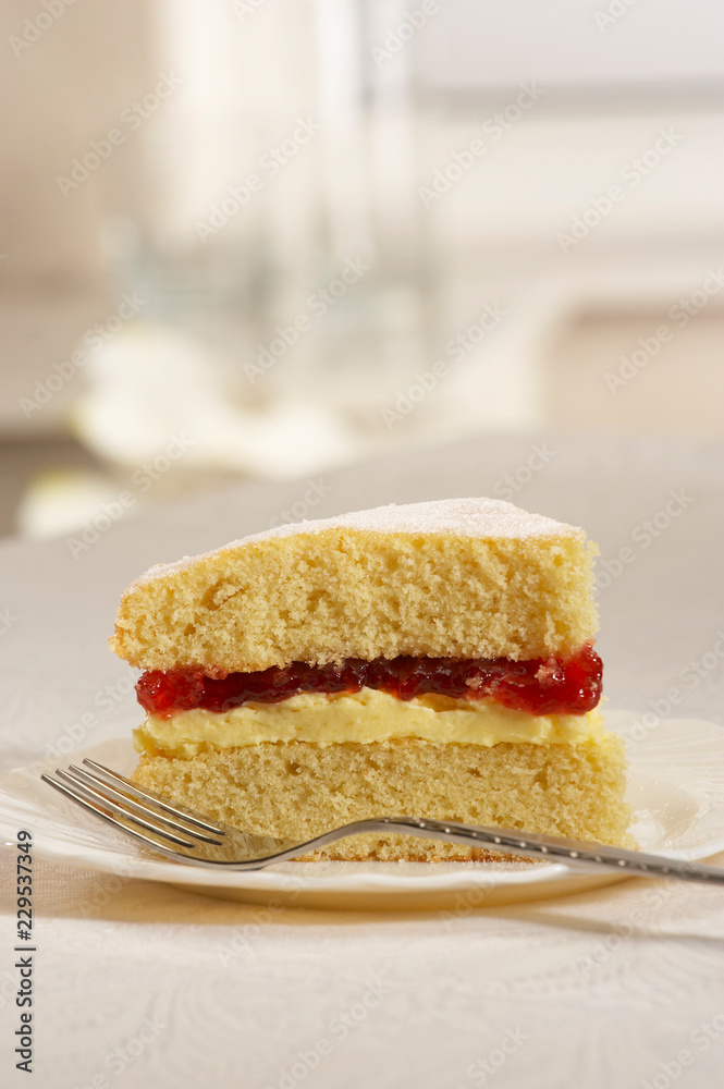 SINGLE SLICE OF JAM AND CREAM SPONGE CAKE ON WHITE PLATE WITH FORK SINGLE SLICE OF JAM AND CREAM SPONGE CAKE ON WHITE PLATE WITH FORK