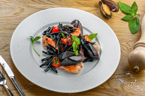 Excellent strozzaperti black squid ink pasta with seafood on a table. Plate of healthy Italian meal with shrimp, mussels and octopus. Top view.
