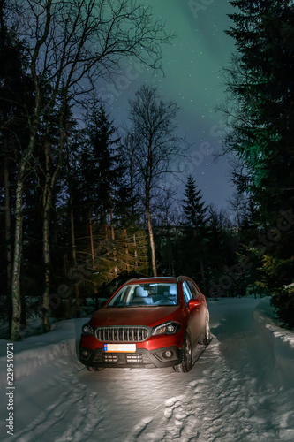 Red car standing on the narrow road in the forest during Northern Lights  Norway.