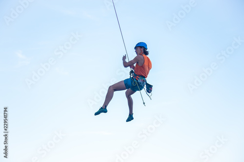 View of man in hardhat hanging on rope while doing rappel and showing pirouettes flying in air 