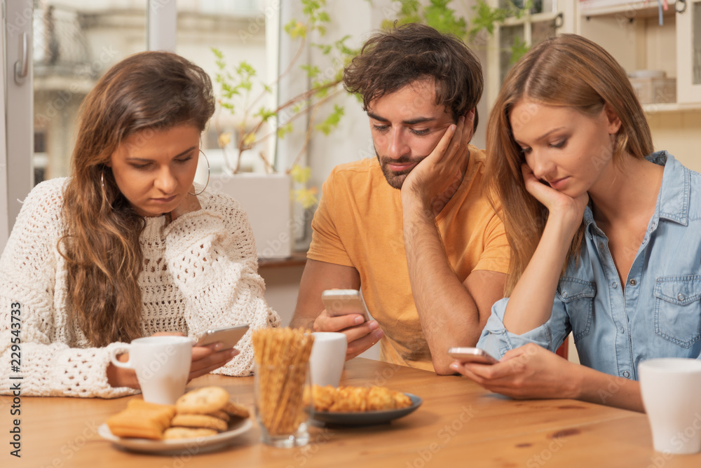 Friends sitting in the kitchen and watching on their phones Friends sitting in the kitchen and watching on their phones