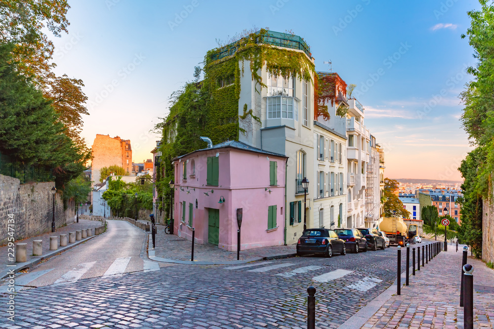 Fototapeta premium Przytulna stara ulica z różowym domem przy słonecznym wschodzie słońca, ćwiartka Montmartre w Paryż, Francja