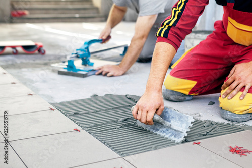 Ceramic Tiles. Tiler placing ceramic wall tile in position over adhesive photo