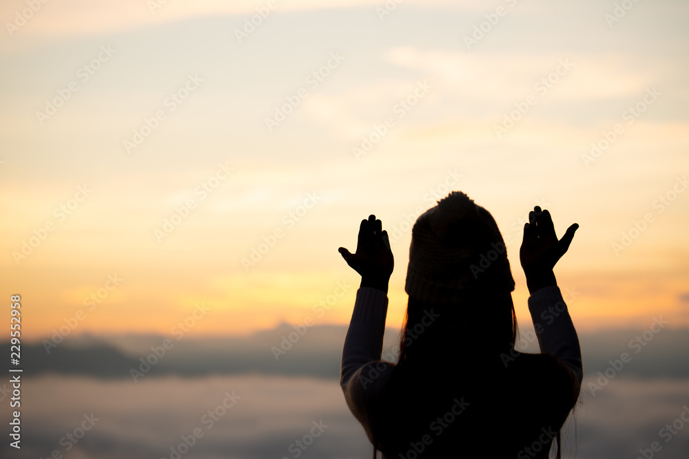 Silhouette of woman praying over beautiful against sunrise background