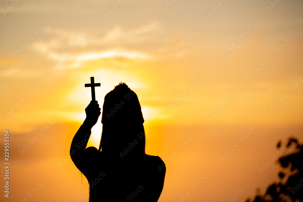 Silhouette of teen girl hands holding wooden cross on sunrise background, Crucifix, Symbol of Faith.