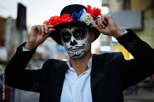 a man with a painted face of a skeleton, a dead zombie, in the city during the day. day of all souls, day of the dead, halloween, ghost walk.