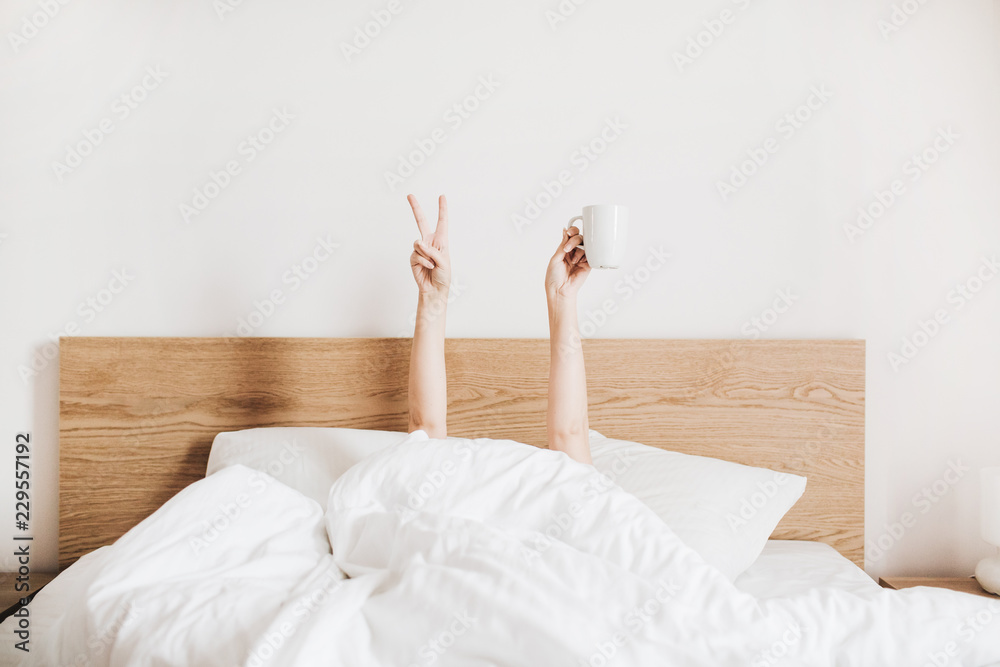 Hand's of young woman with coffee mug in bed with white linens. Minimal happy morning concept. - obrazy, fototapety, plakaty 