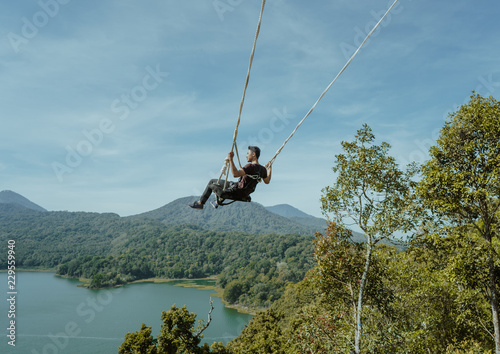 young asian man swinging from high top hill